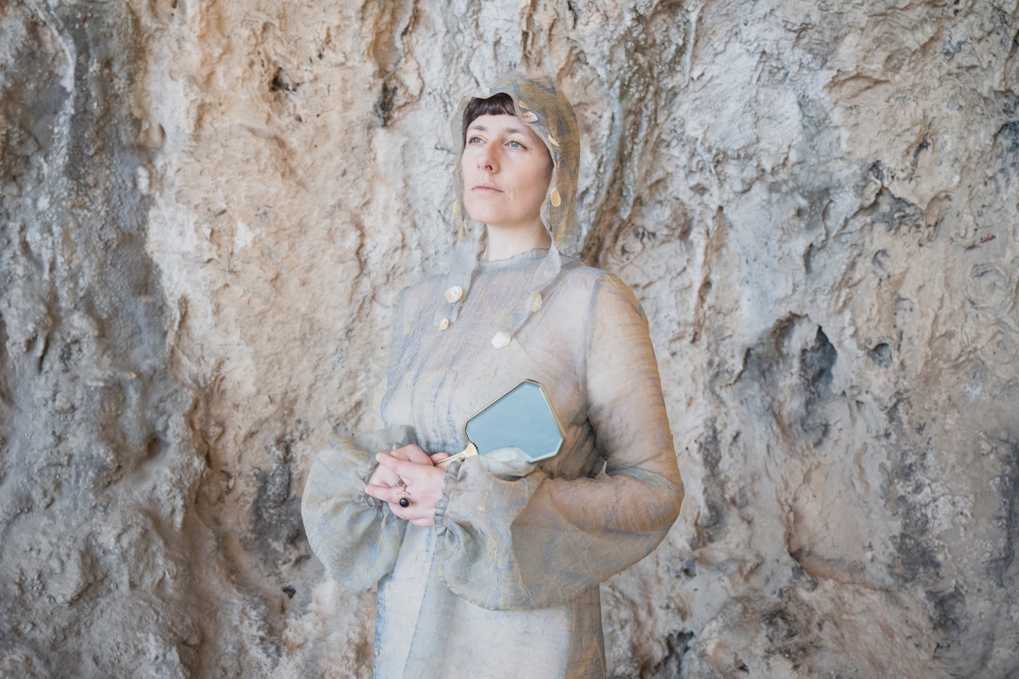 Jolanda Moletta in a sheer hooded dress against a cave wall