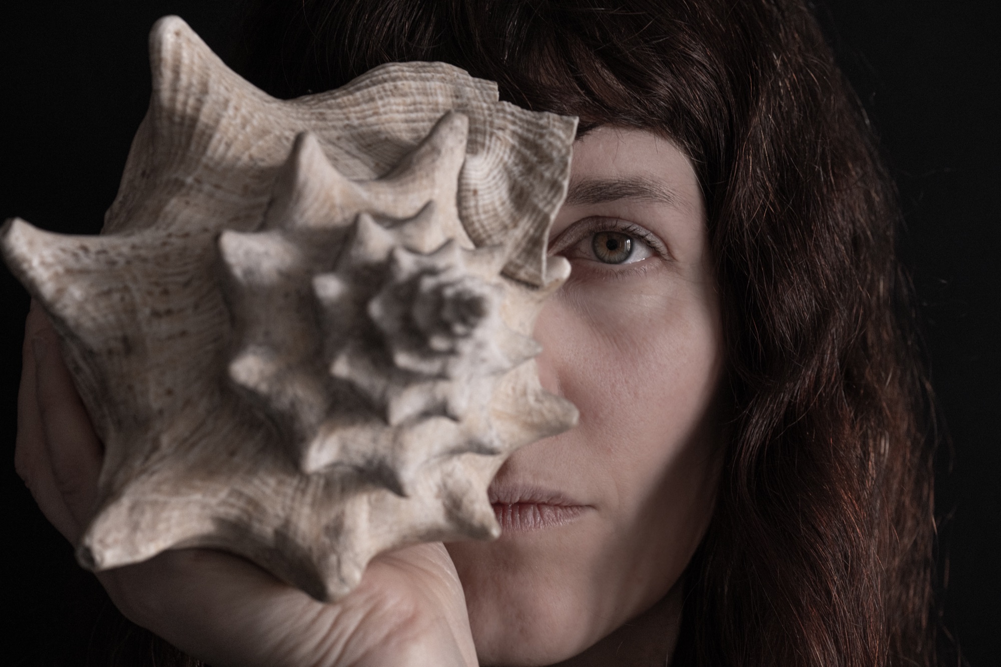 Jolanda Moletta holding a conch shell over half her face